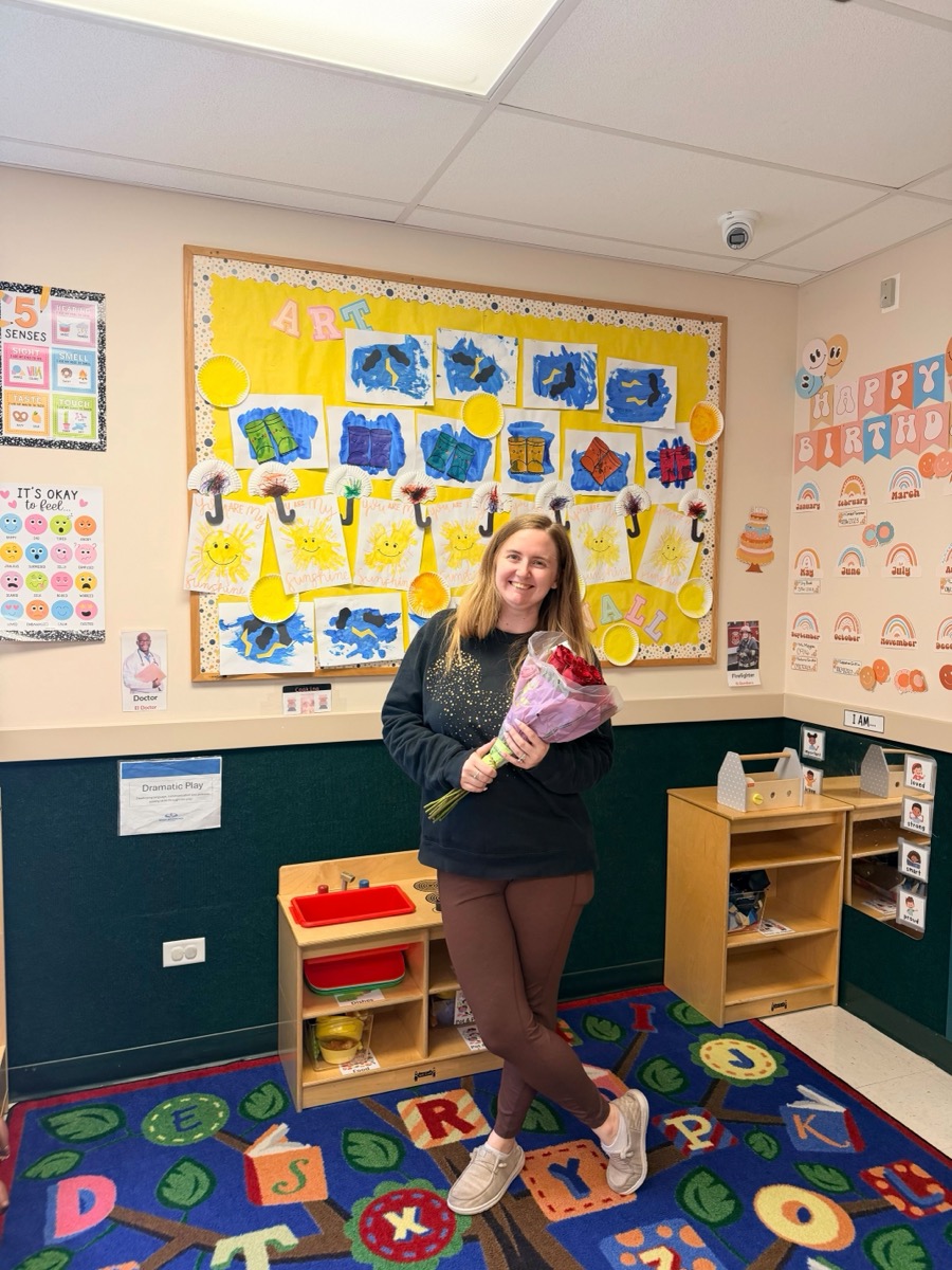 A teacher smiling in her classroom holding her bouquet of roses